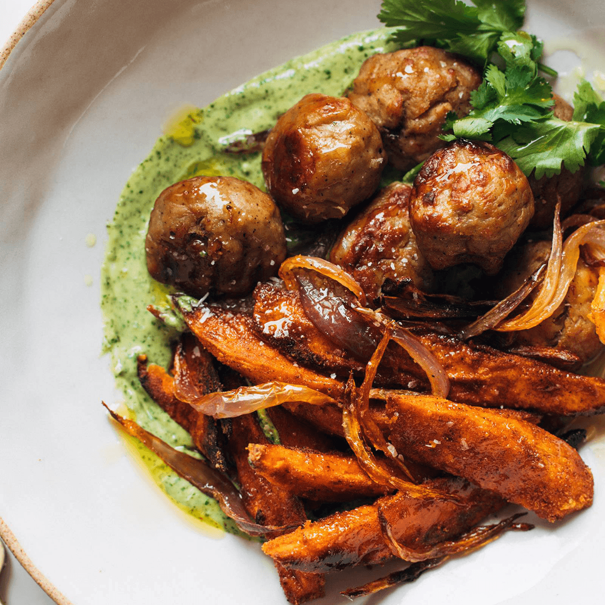 Meatballs and sweet potatoes in a bowl with aji verde.